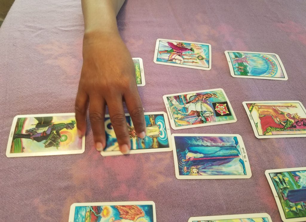 A tarot card spread on a mauve background with a brown hand extending from the top to cover one of the cards